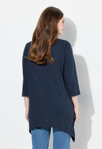 Marinblå topp med trekvartsärmar och avslappnad passform, med en något längre nederdel bak och sidslitsar för ökad rörelsefrihet.