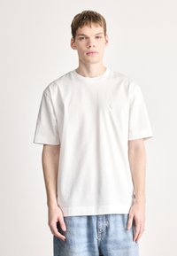 Tricou alb cu mâneci scurte, realizat din bumbac moale. Decolteu rotund, design simplu, cu un mic logo circular pe piept.