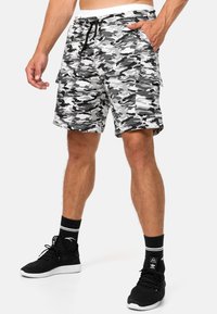 Shorts cargo gris en camouflage avec une taille élastique à cordon, poches latérales et en tissu mélangé de coton. Associés à des chaussures de sport noires.