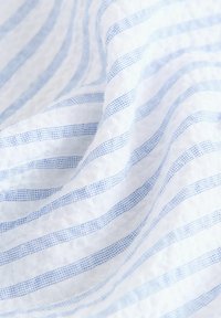 Baumwollstoff mit weißem Hintergrund, der horizontale hellblaue Streifen und eine strukturierte Webart aufweist, was ein weiches, schichtartiges Erscheinungsbild erzeugt.