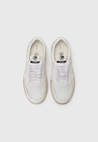 Zapatillas blancas de cuero suave, con detalles perforados, suela de goma beige, cordones planos y un logo en la lengüeta.