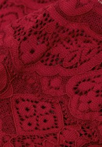 Tissu en dentelle rouge présentant des motifs floraux et géométriques intricats, avec une surface texturée et des détails en tissage ouvert, mettant en valeur le savoir-faire.