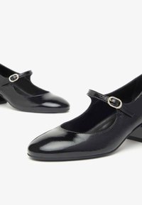 Schwarze Lackleder-Mary-Jane-Schuhe mit runder Zehenpartie, flachen Blockabsätzen und einem schmalen Riemen mit dekorativer Schnalle.