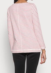 Maglia a maniche lunghe a righe rosse e bianche con scollatura rotonda, caratterizzata da una cucitura centrale e dettagli con bottoni lungo la schiena.