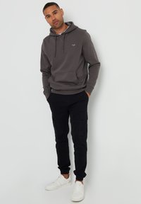 Grijze hoodie met een frontzak, capuchon met trekkoord en geborduurd logo, gecombineerd met zwarte cargobroek en witte sneakers.