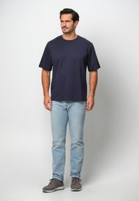 Marinblå bomullströja med kort ärm, kombinerad med ljusblå jeans och grå sneakers. Enkelt mönster, inga synliga mönster eller logotyper.