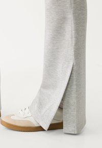 Šedé sportovní kalhoty s měkkou texturou, s postranními rozparky na lemu. Spárované s bílými a béžovými teniskami s gumovou podrážkou.