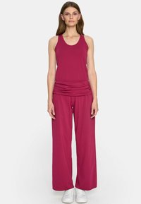 Fuksjowy top na ramiączkach z okrągłym dekoltem, zestawiony z szerokimi fuksjowymi spodniami z marszczonym pasem, oba wykonane z miękkiego, rozciągliwego materiału.