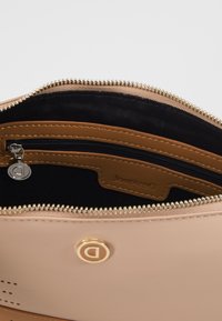 Beige kožená kabelka uvnitř s kapsou na zip, černým podšívkou a zlatými akcenty. Logo návrháře viditelné na kapse.