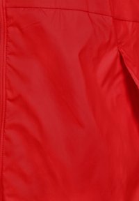 Veste rouge légère avec une texture douce et une finition froissée, dotée d'une fermeture éclair sur toute la longueur à l'avant. Design minimaliste.