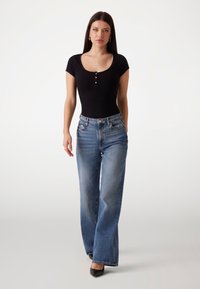 Svart ribbet bodysuit med rund halsringning og korte ermer, kombinert med lyseblå vide jeans. Svart høyhælte sko fullfører antrekket.