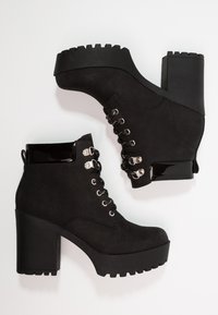 Black ankle boots with a chunky block heel, suede material, and metal eyelets. Features a glossy black accent at the top and textured sole.