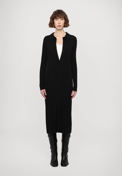 Svart ribbat stickat klänning med krage, hel-längds knappstängning och åtsittande silhuett. Svarta höga stövlar fulländar outfiten.