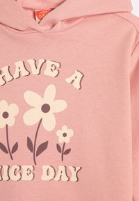 Różowy sweatshirt z kapturem z graficznym motywem kwiatu z kremowymi płatkami i ciemnobrązowymi liśćmi, tekst brzmi "MIŁEGO DNIA" w zabawnym stylu.
