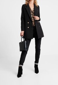 Czarna marynarka dwurzędowa na panterkowej bluzce, w zestawie z czarnymi spodniami ze ściągaczami w paski oraz czarnymi botkami na obcasie. Czarna torebka.