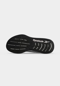 Μαύρη λαστιχένια σόλα παπουτσιού Reebok που δείχνει υφασμένα μοτίβα πέλματος και το λογότυπο Reebok σε λευκό σε απλό ανοιχτό γκρι φόντο.