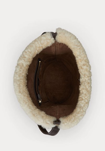 Brun mockaväska med ett mjukt krämfärgat foder i konstgjord lammull, oval form, ficka med dragkedja och en mörkbrun rem, sedd ovanifrån.