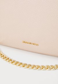 Geantă de mână din piele texturată roz, cu o curea din lanț aurit și logo-ul embosat "MICHAEL KORS" pe față.