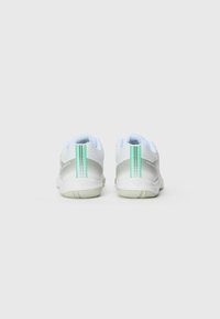 Des chaussures de sport blanches avec une tige lisse en argent et en maille, arborant une bande d'accent verte et une semelle en caoutchouc texturée.