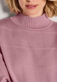 Helles rosa Rollkragensweater mit geripptem Kragen und horizontalen Strickmustern. Weiche Textur und entspannte Passform.