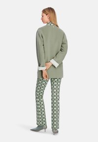Hellgrüner Wollmischblazer mit klassischem Schnitt, kombiniert mit gemusterten Hosen mit geometrischem Design in Grün und Schwarz.