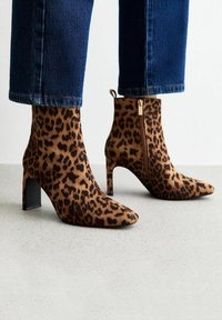 Botines de tobillo de estampado de leopardo con punta afinada, material texturizado suave y tacón cuadrado negro. Detalle de cremallera lateral para un uso fácil.