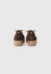 Brown suede sneakers with beige rubber soles, featuring a rounded shape, metal hardware accents, and brown laces.