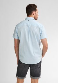 Cămașă bleu deschis cu mânecă scurtă, dintr-un material respirabil, având guler cu nasturi și plisă la spate. Asortată cu pantaloni scurți negri cu manșete rulate.