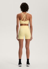 Rumena atletska športna modrc in ustrezne kratke hlače, ki imata križane naramnice in prilegajoč dizajn. Gladek material z minimalnimi detajli.