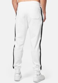Vita sweatpants med svarta sidostråk, elastisk midja och en bakficka. Tillverkade av mjukt material för komfort och avslappnad användning.