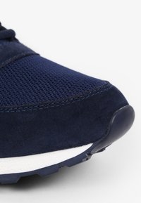 Marineblauwe sportschoen met een bovenwerk van mesh en suède accenten, voorzien van een gestructureerd oppervlak en een witte tussenzool voor contrast.