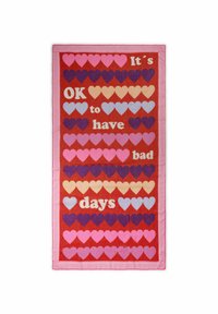 Tissu rectangulaire rouge, présentant plusieurs rangées de cœurs de couleurs variées, avec un texte blanc indiquant : "C'est normal d'avoir des jours mauvais." Bord rose.