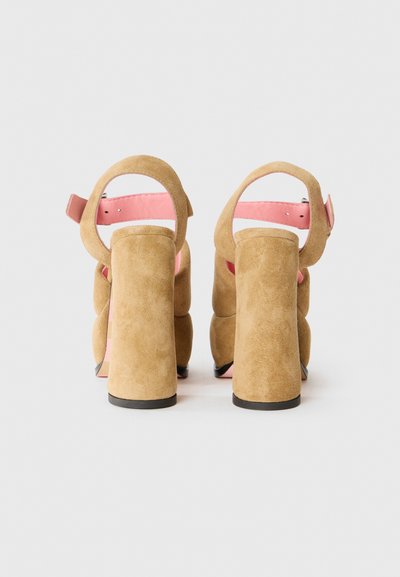 Tan mockask högklackade sandaler med en kraftig klack, öppen baksida och ett rosa band. Har en slät yta och rundade detaljer.