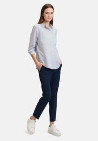 Button-up shirt with blue and white stripes, long sleeves; paired with navy slim-fit pants and white sneakers. Simple, casual outfit.