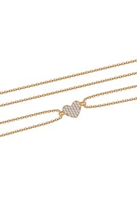 Naszyjnik w kolorze złotym, składający się z trzech delikatnych łańcuszków, z zawieszką w kształcie serca ozdobioną białymi kamieniami, tworzącą lśniący efekt.