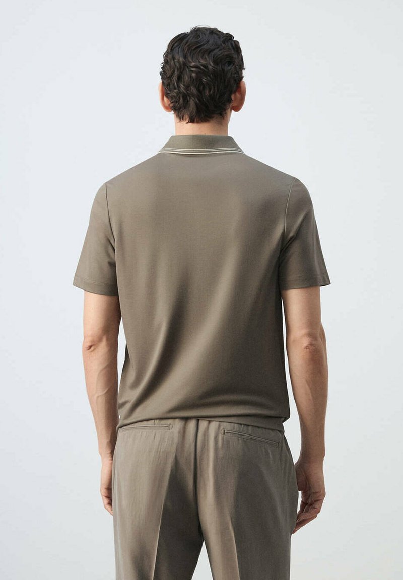 Man with short curly hair shown from behind, wearing a short-sleeve olive polo shirt and matching pants, standing against a plain background.