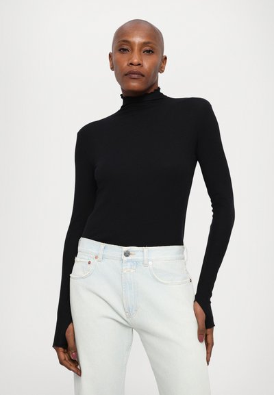 Top negro de manga larga y cuello vuelto con una textura suave, combinado con unos vaqueros de tiro alto en azul claro que cuentan con un diseño clásico de cinco bolsillos.