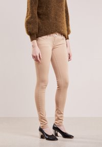 Beiga skinny jeans med en slät yta, med framdragkedja och knappstängning, kombinerat med svarta högklackade skor med glänsande detaljer.