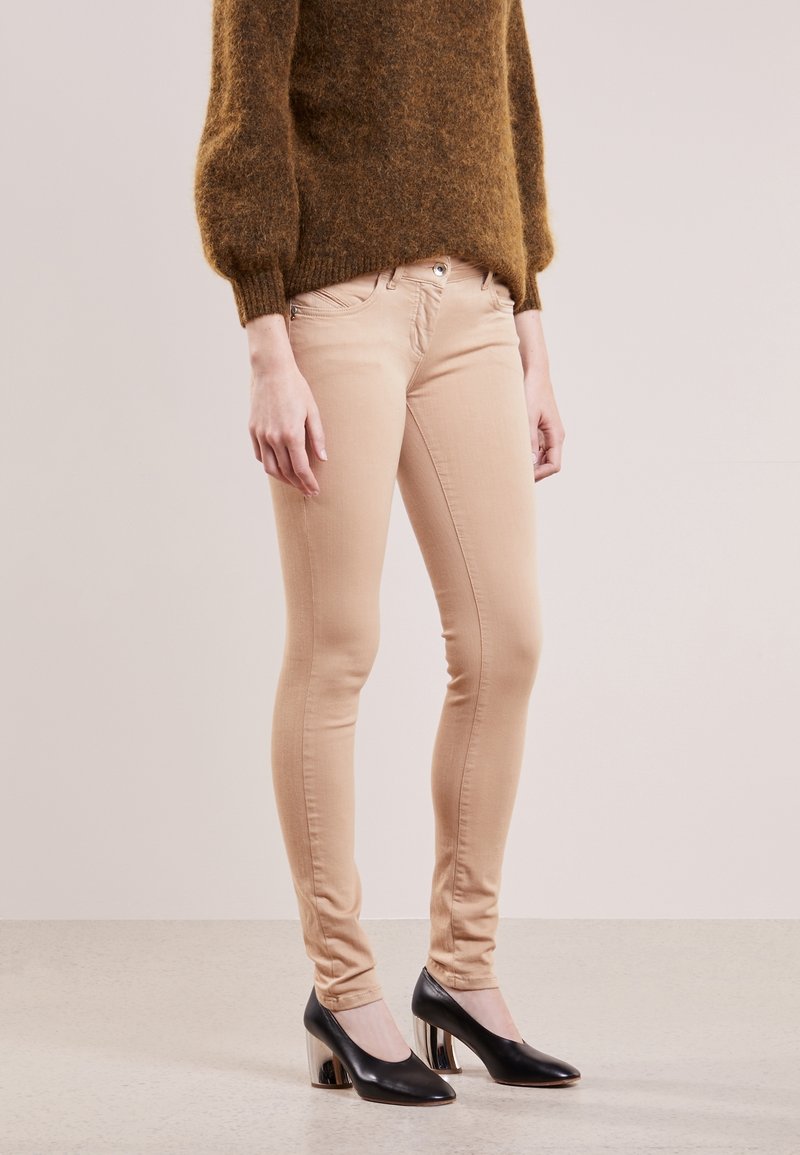 Beiga skinny jeans med en slät yta, med framdragkedja och knappstängning, kombinerat med svarta högklackade skor med glänsande detaljer.