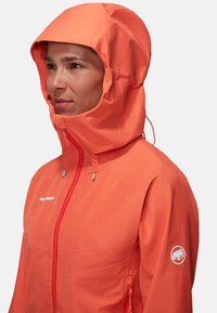 Vandafvisende orange jakke med lynlås foran, justerbar hætte og logo patch på ærmet. Har to sidelommer og en slank, glat tekstur.