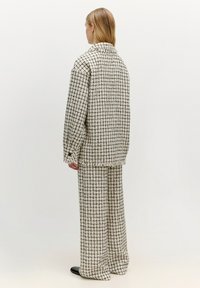 Geweven twee-delig outfit in crème met een zwart roosterpatroon. Bevat een loszittende jas en wijde broekspijpen. De stof heeft een gestructureerde afwerking.