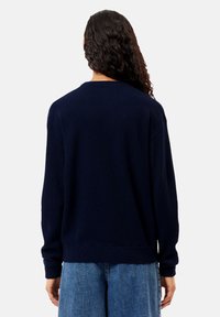 Maglione lavorato a maglia di colore blu navy con colletto a girocollo, spalle basse e polsini a coste. Texture morbida e vestibilità rilassata, abbinato a denim chiaro.