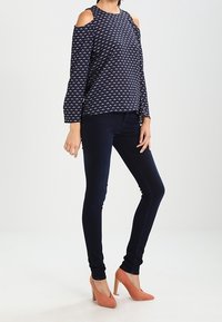 Navy top with cold shoulders, geometric pattern, and bell sleeves paired with dark skinny jeans and light pink high heels.