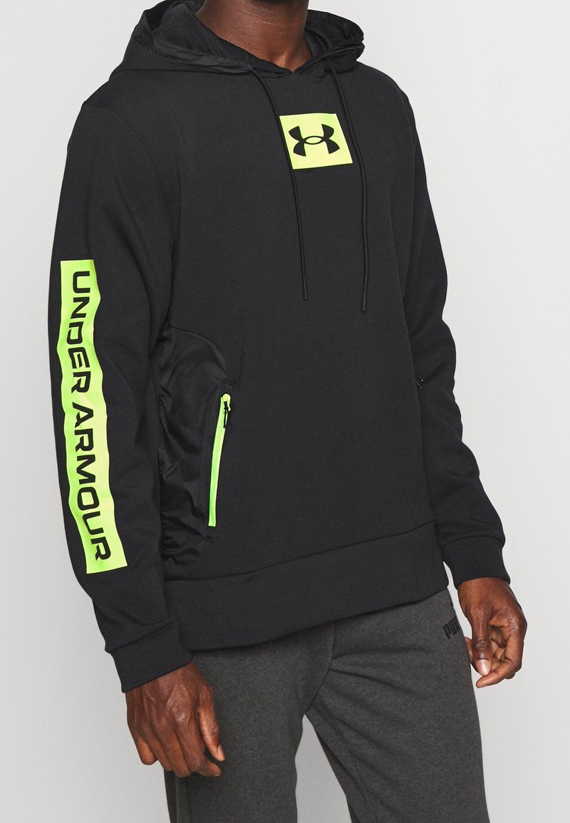 Felpa con cappuccio nera dotata di un grande logo verde neon sul petto e sulla tasca laterale, con il testo in grassetto "UNDER ARMOUR" sulla manica.