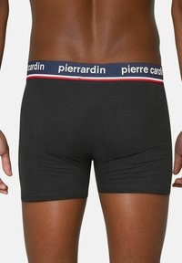Zwarte katoenen boxershorts met een marineblauwe tailleband waarop in witte letters "pierre cardin" staat en rode accentlijnen. Glad materiaal en een aansluitend ontwerp.