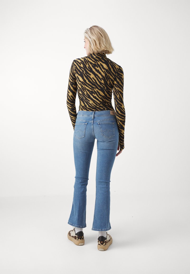 Haut à rayures tigre noir et marron à manches longues associé à un jean flare bleu clair, avec une taille ajustée et des chaussures décontractées à imprimé léopard.
