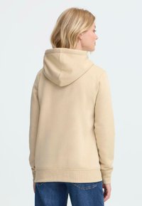 Felpa in cotone beige con cappuccio regolabile e polsini a coste. Tessuto liscio, vestibilità casual e design semplice, abbinata a jeans blu.