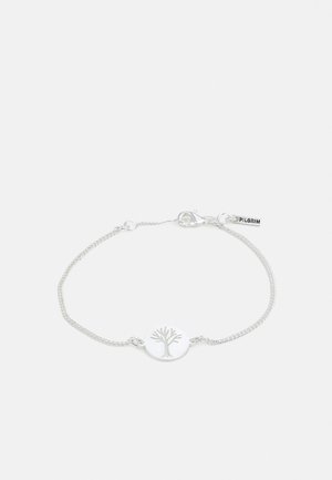 Bracelet en argent avec une chaîne délicate, équipé d'un pendentif circulaire avec un motif d'arbre et une étiquette de logo. Design simple et minimaliste.