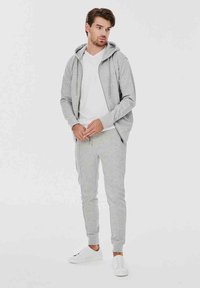 Szary sweatshirt z kapturem i zamkiem, w połączeniu z dopasowanymi dresami i białą koszulką typu V-neck. Białe sneakersy dopełniają stylizację.