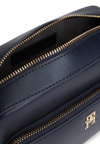 Sinine nahkkott kullast lukustustega ja silmapaistva metallist logoga. Omab siledat välispinda ja tekstuuriga luku detaile.